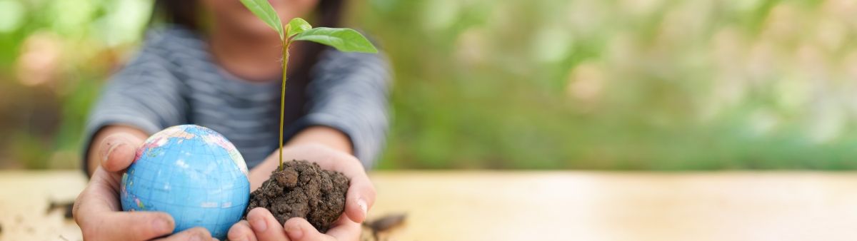 A child holds a small seedling in one hand and a small globe in the other. 