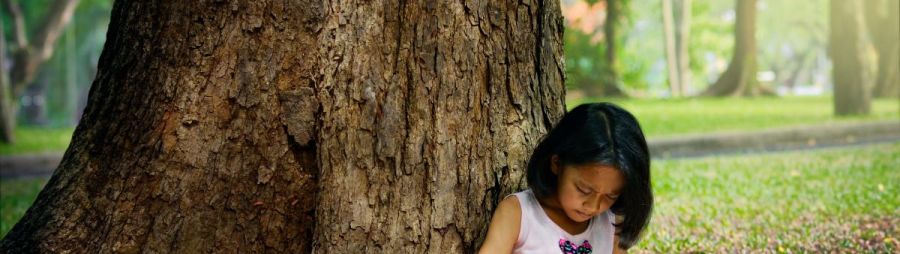 young child doing homework under a large tree