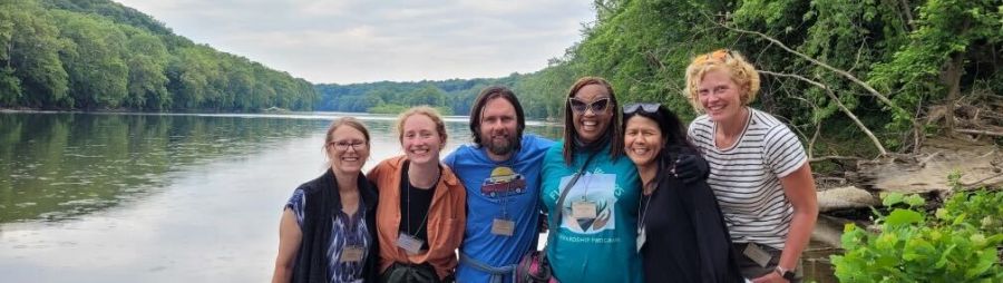 A group of people posing for a picture in front of a body of water and forest