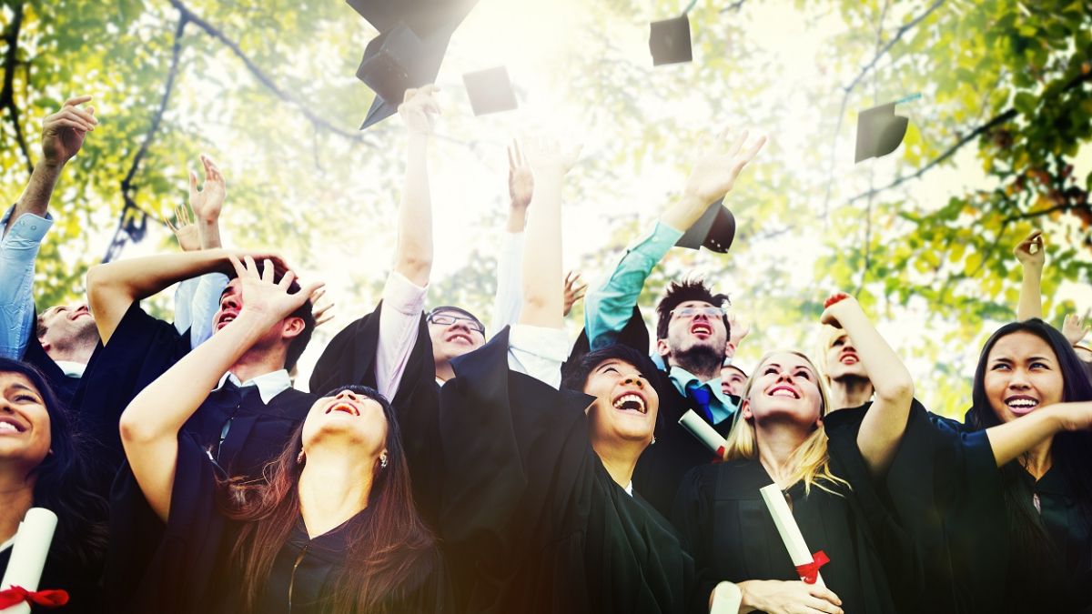 graduates in caps and gowns looking up with sunshine and trees above
