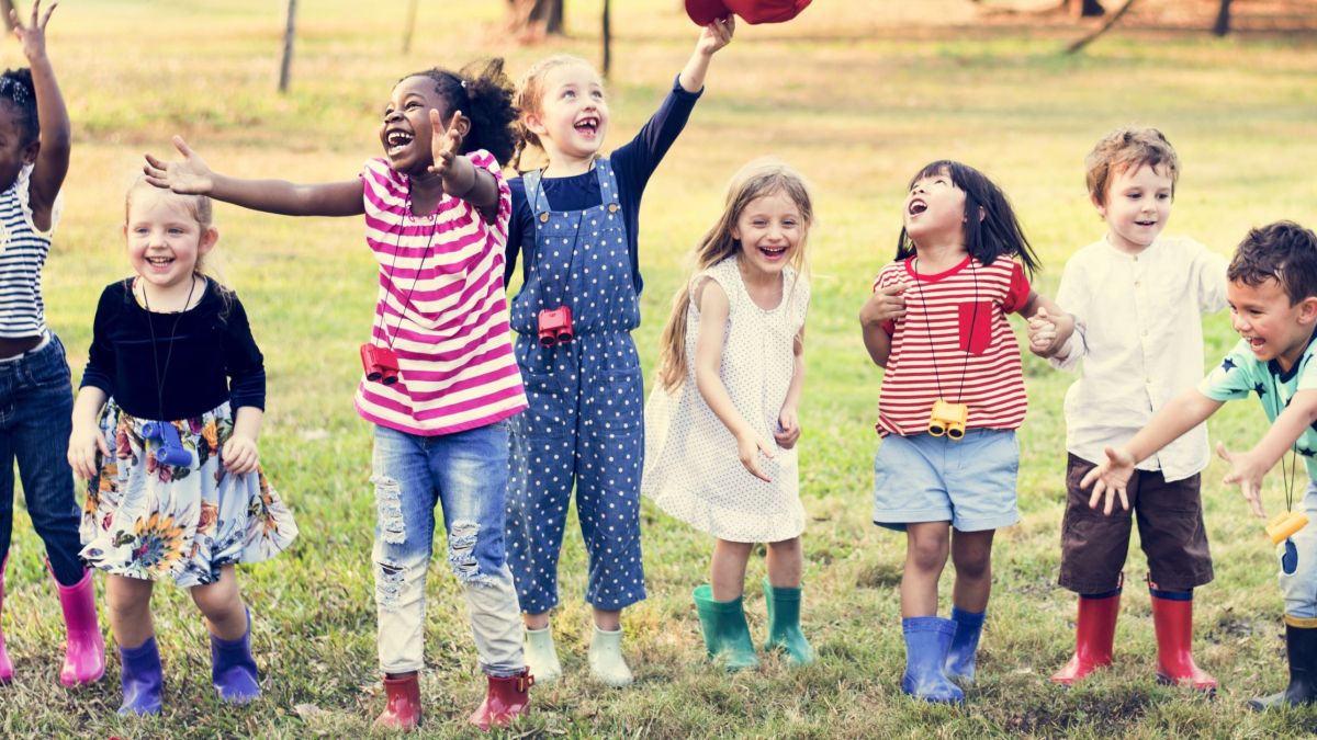 Preschool aged children outside lined up horizontally, jumping and laughing 