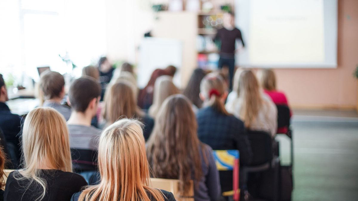 teacher stands in front of high school students, is blurred out