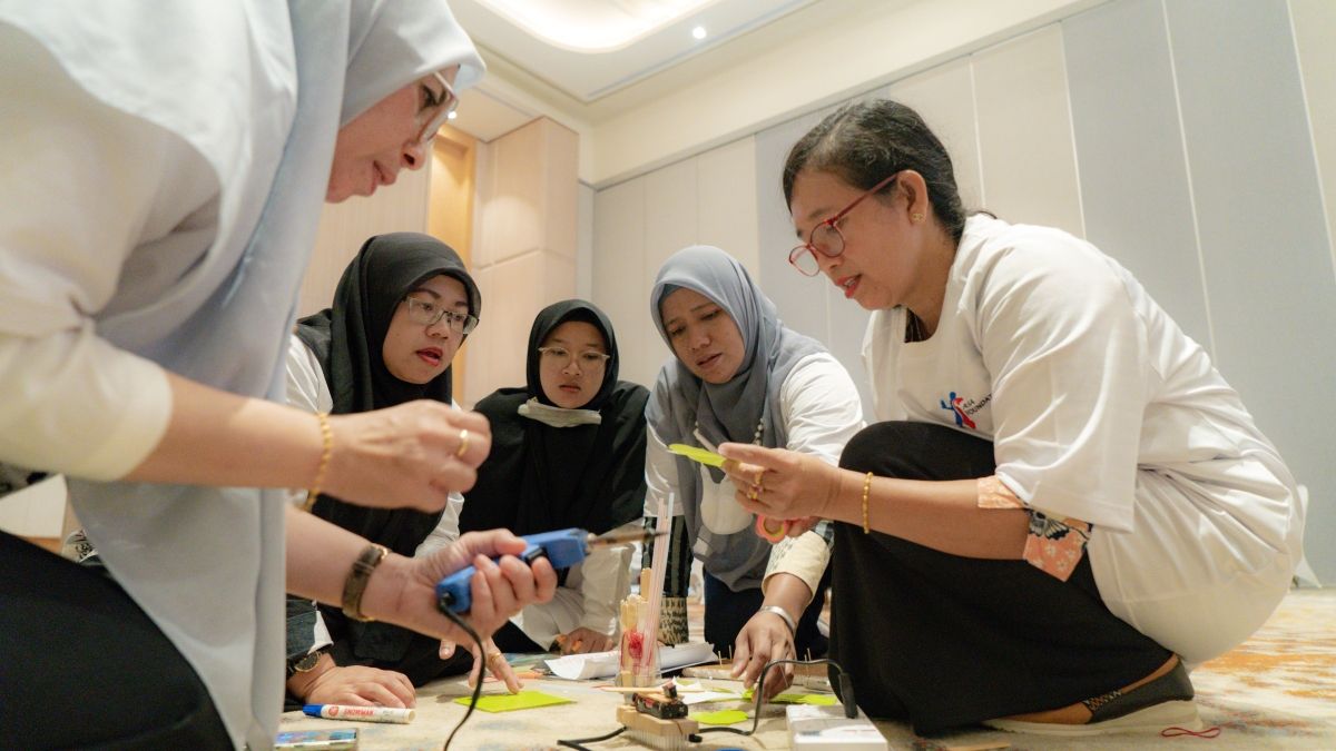 A group of Indonesian women kneeling on the floor in a group working on a STEM kit