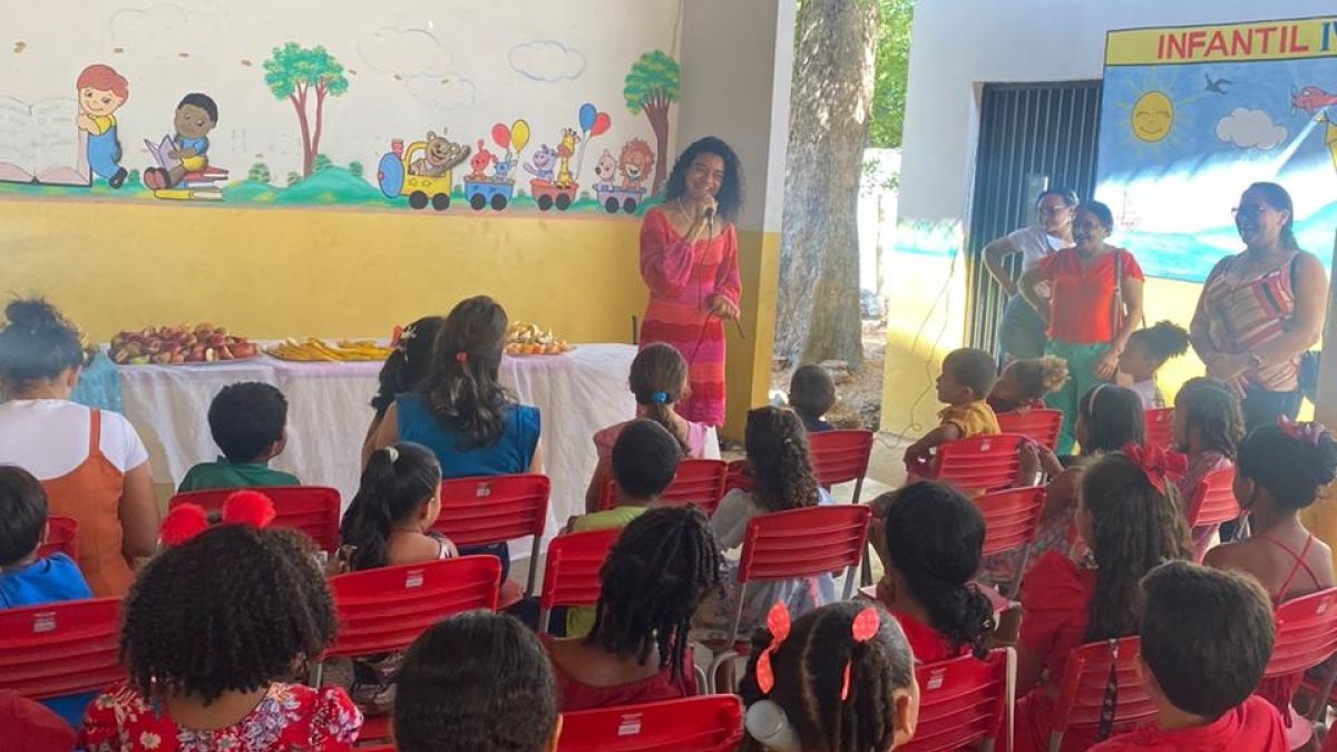 A young woman speaking in front of a classroom full of students in red uniforms