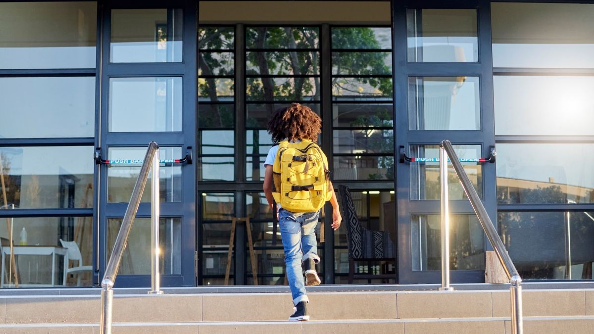 Child, walking and school entrance for education, learning or childhood development at academy building. Kid having a walk up the steps ready for back to school morning with backpack for knowledge