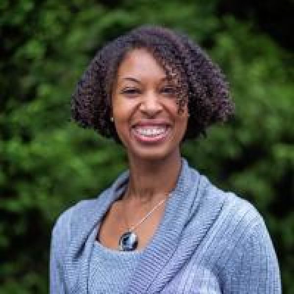 black woman wearing a light blue blouse and cardigan smiling at the camera
