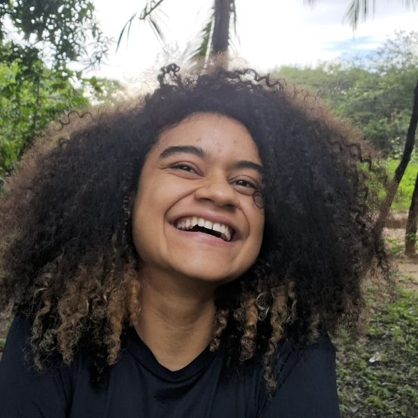 A woman smiling outdoors under trees