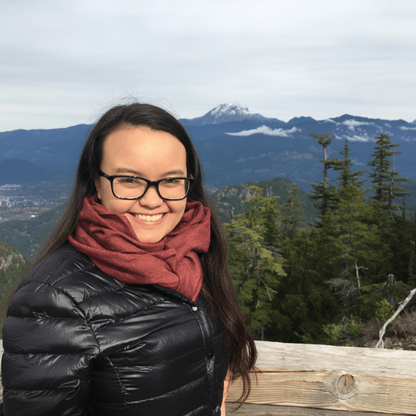 Woman with a black coat and scarf outside with mountain scenery