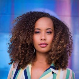 Danni Washington wearing a multicolored striped blouse in front of blue and pink background