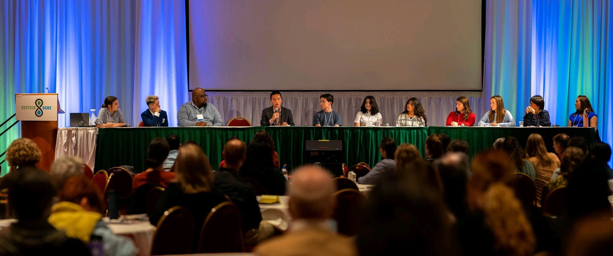 Ten panelist on stage sitting in front of a large audience. 
