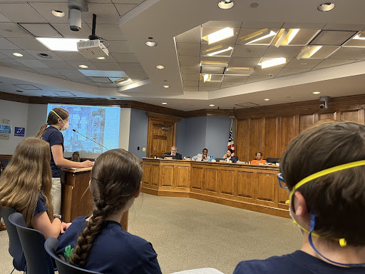 Student stands at a podium in a local government meeting setting