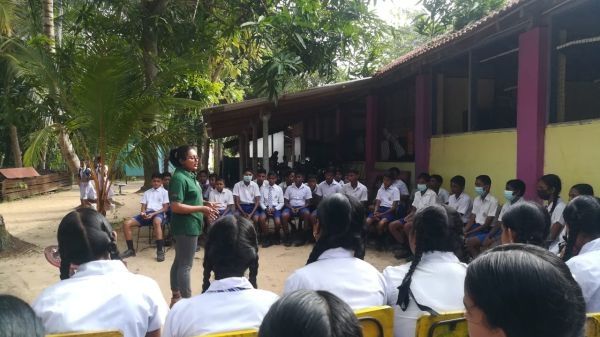 Children sitting outside listening to a teacher. 