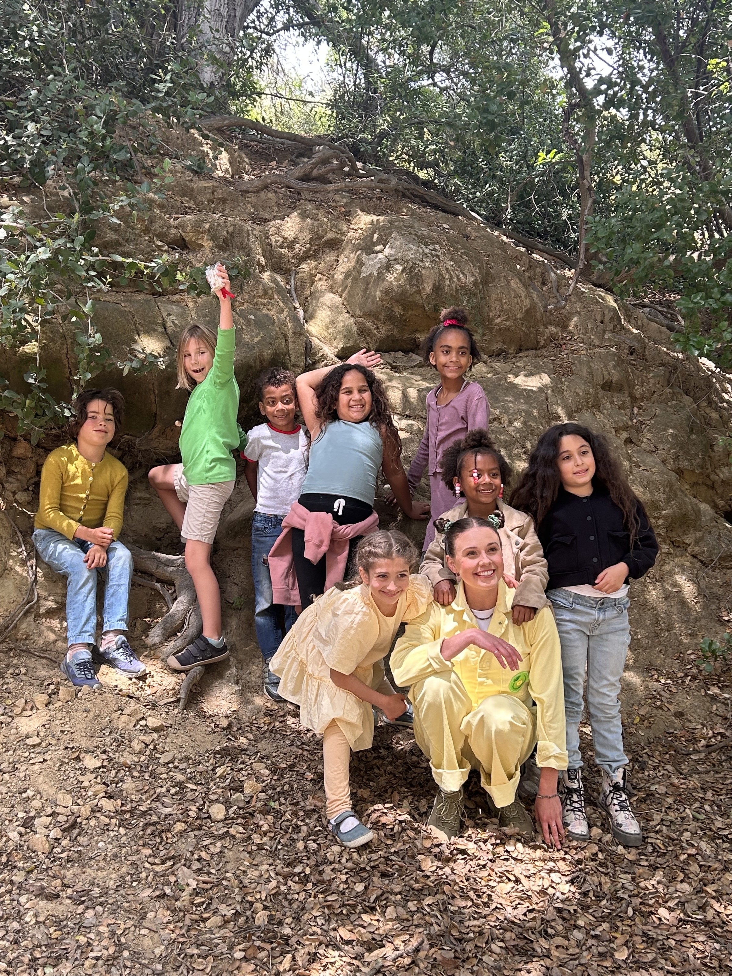 A group of small children posing near a tree in a wooded area.