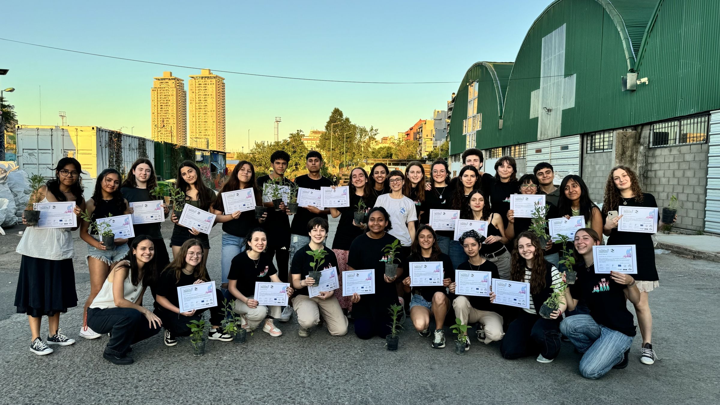 A group of young students posing with certificates and plants.