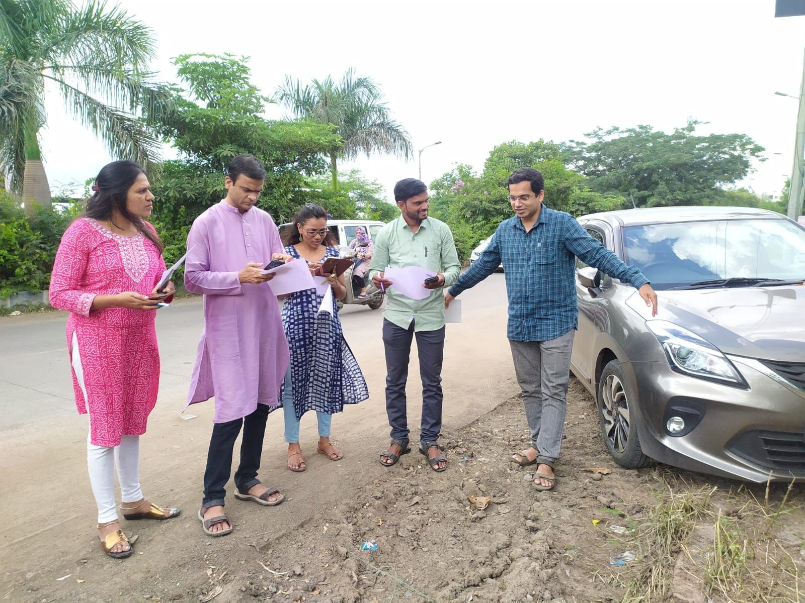 Avadhut speaking with adults outdoors referencing papers
