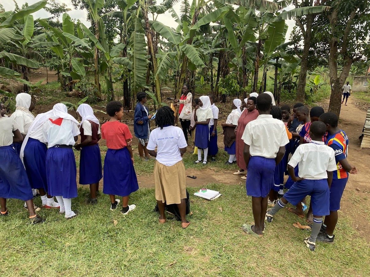 Schoolchildren listening to a talk outside next to banana trees