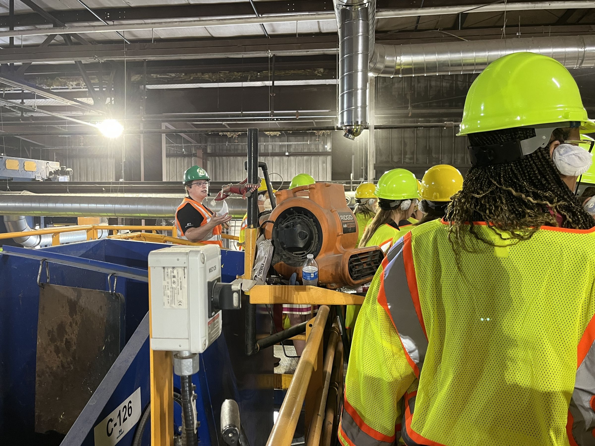 Sagan with adults in hardhats inside a recycling facility