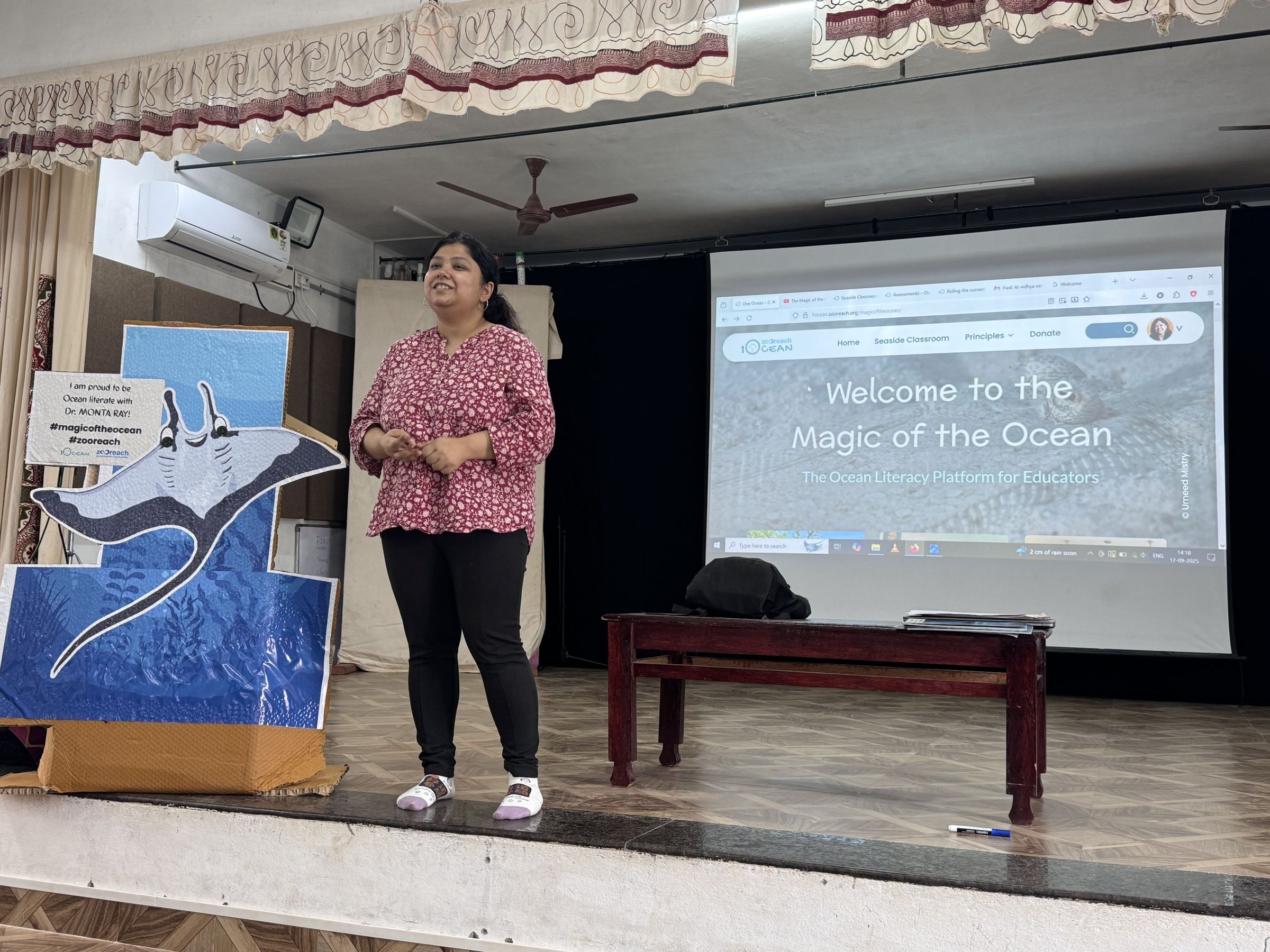 Tandrali talking on a stage with a large cartoon image of a manta ray