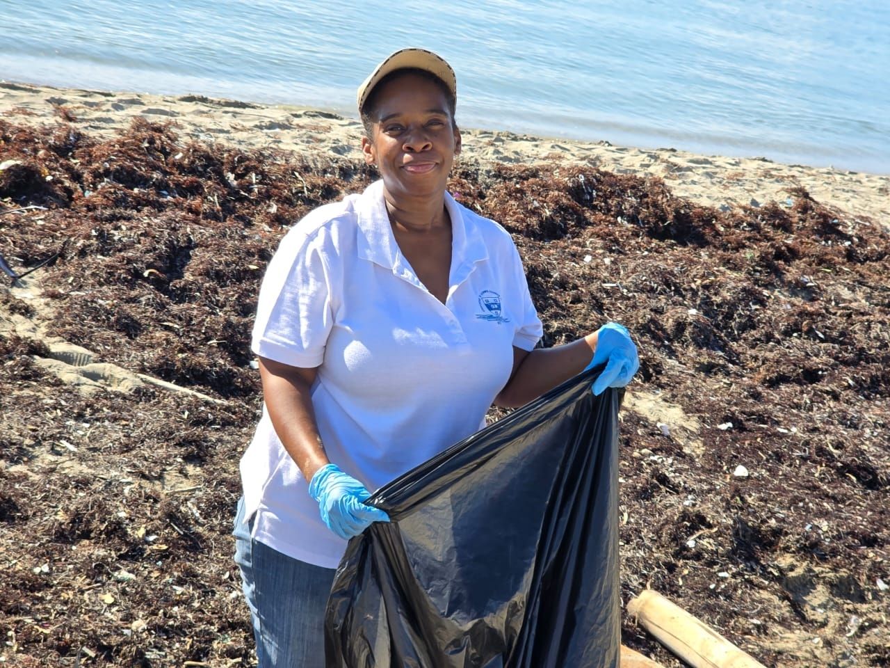 CEE-Change Fellow Nicole wearing blue gloves and holding a trash bag on a beach