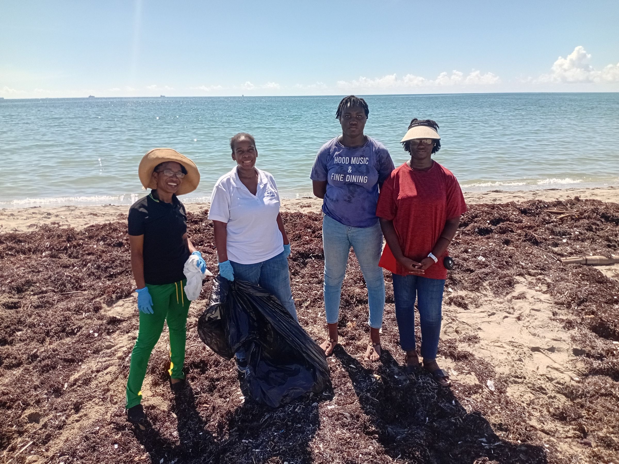 A group of four people stand in front of the ocean on a seaweed-covered beach.
