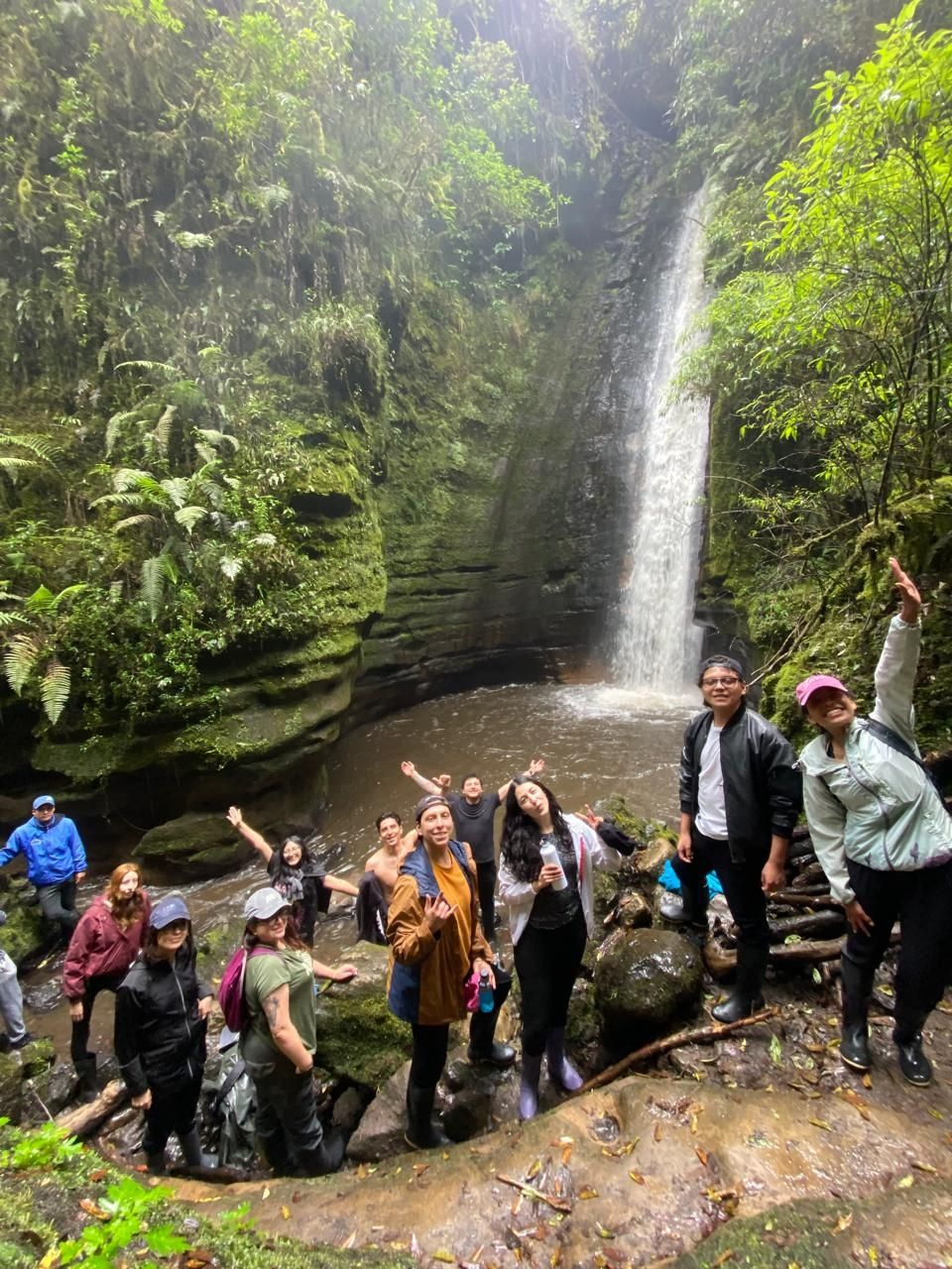 A group poses in a forested area in front of a waterfall