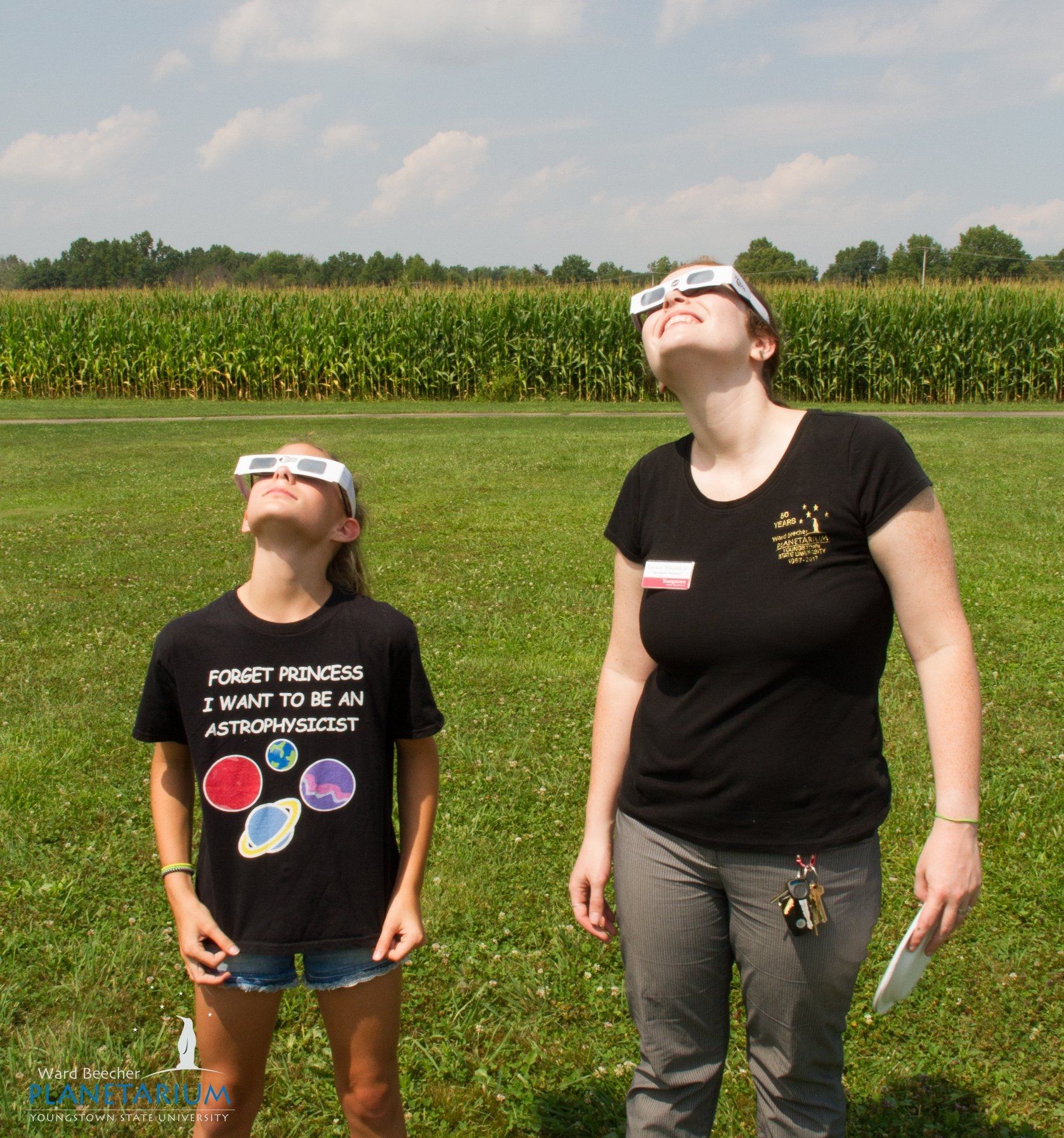 A child and person look up to the sky with protective glasses on.