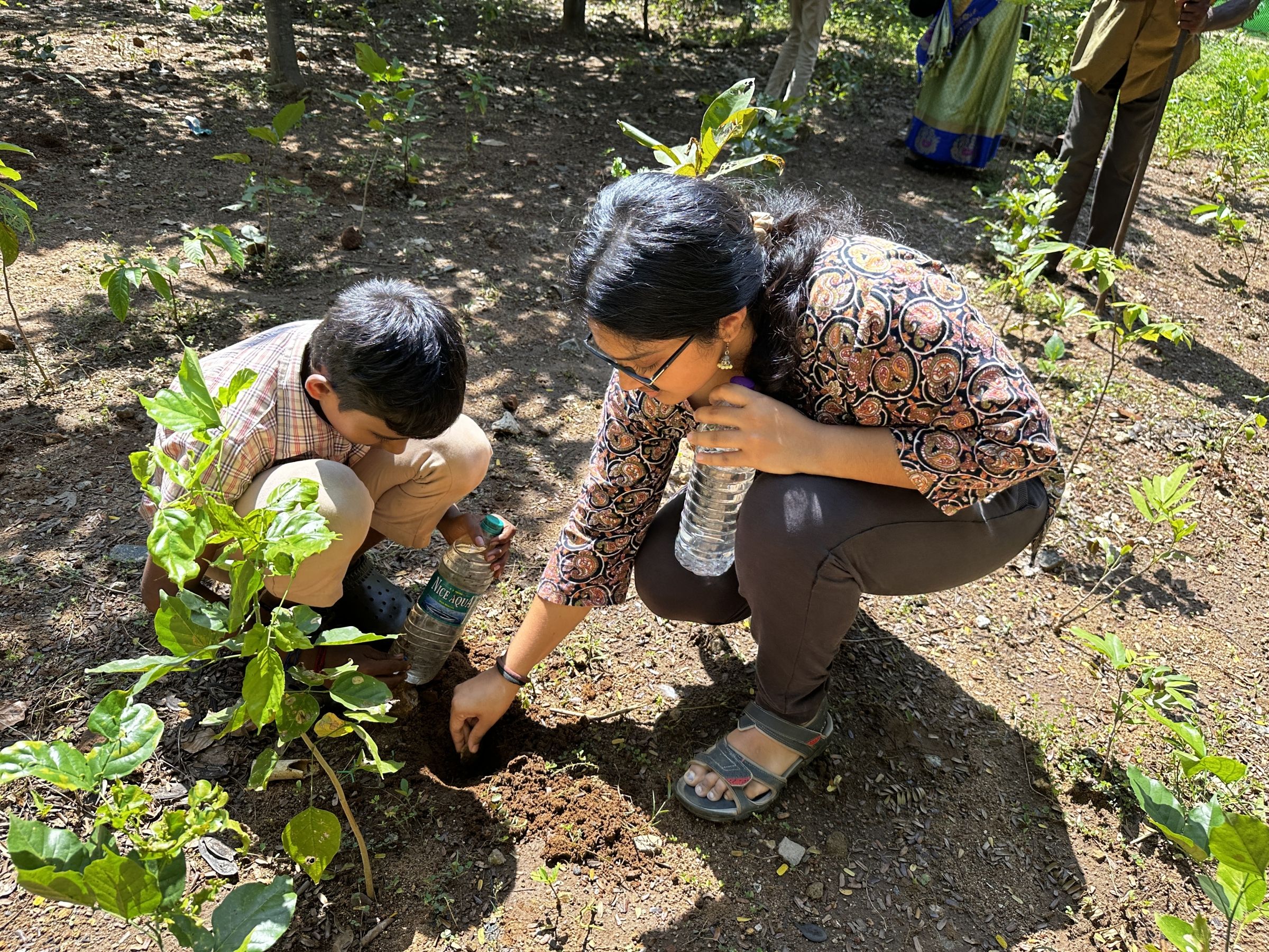 Anooja kneeling on the ground outside with a young child
