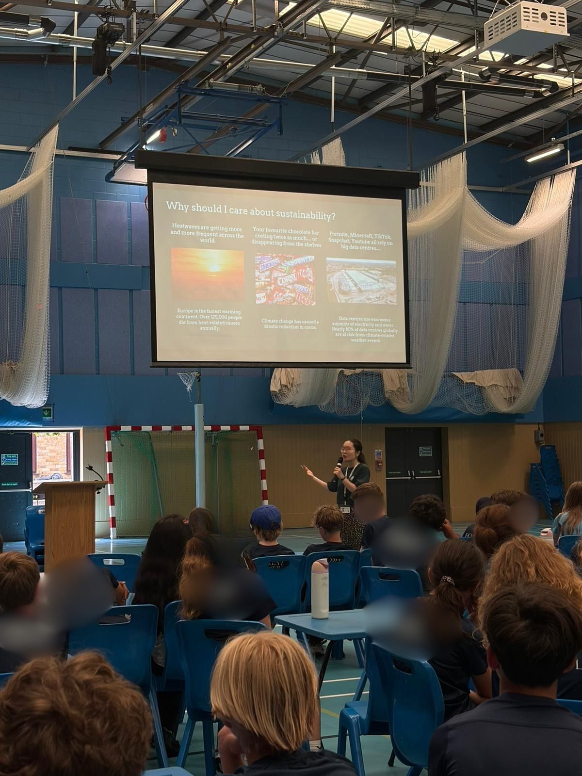 Belidna holds a microphone and presents below a large projector screen to an audience