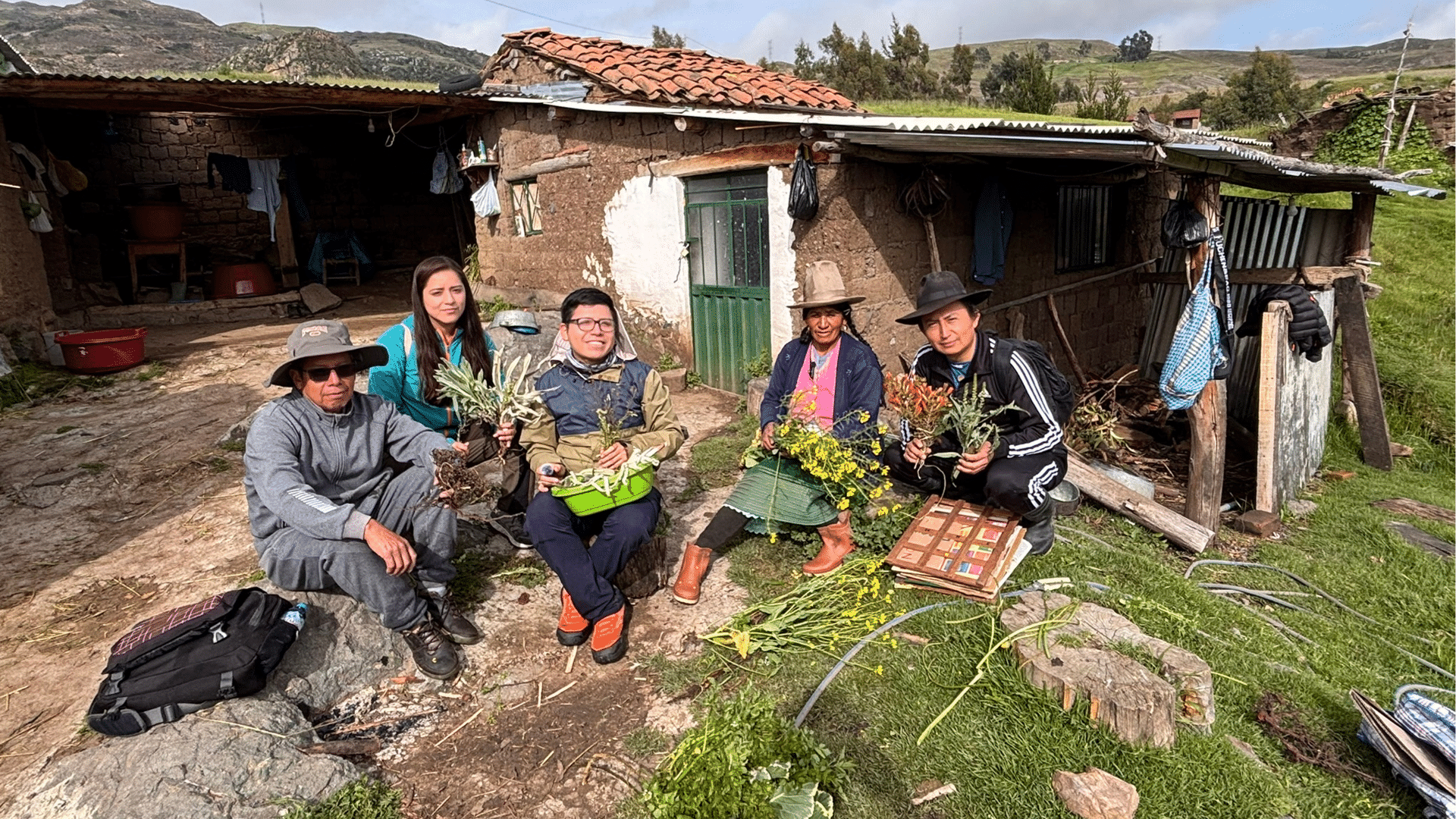 Adrian and other people hold plants and pose for a photo outside of a house in the Peruvian mountains