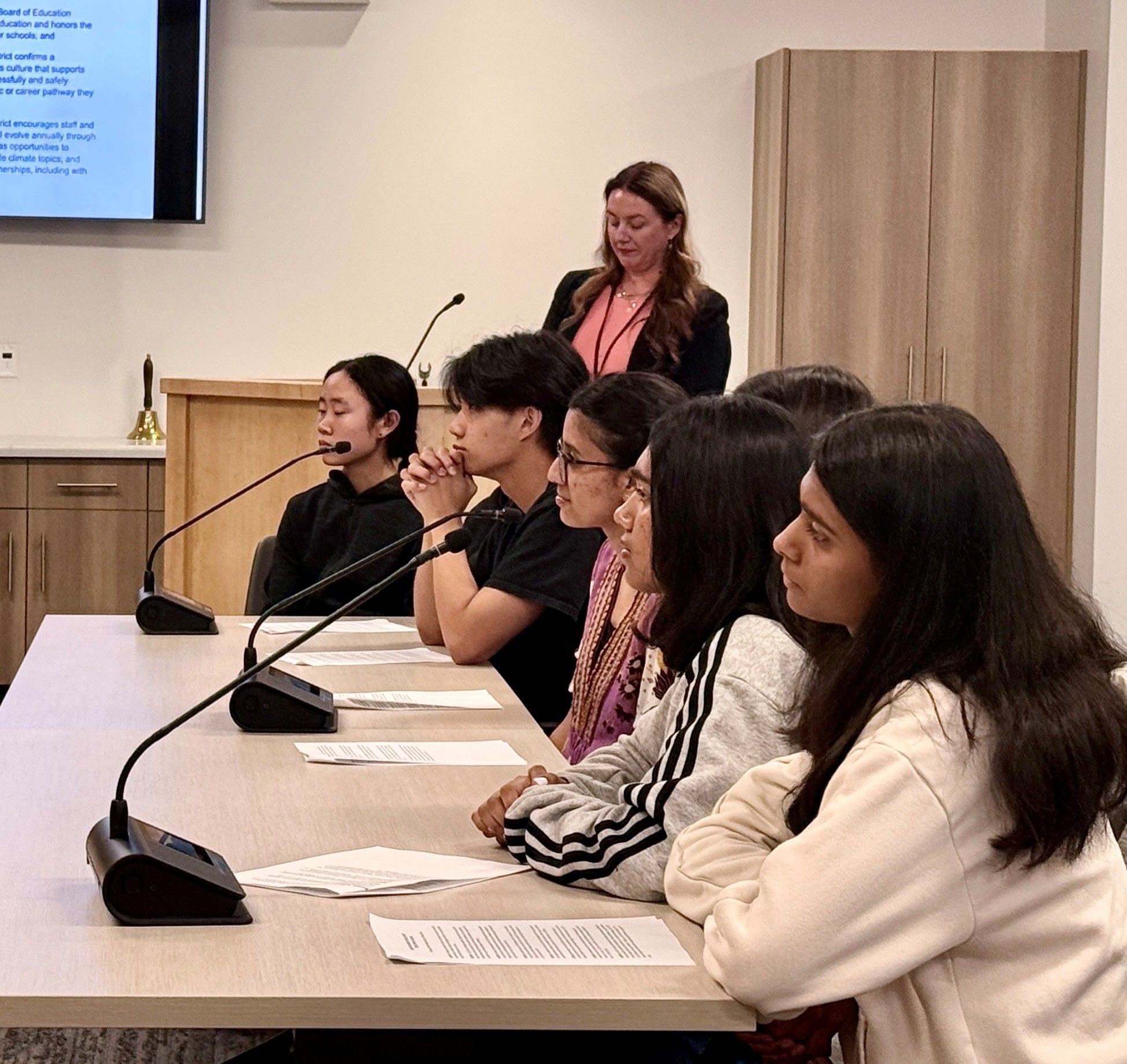 A group of students sitting in front of microphones at school district board meeting