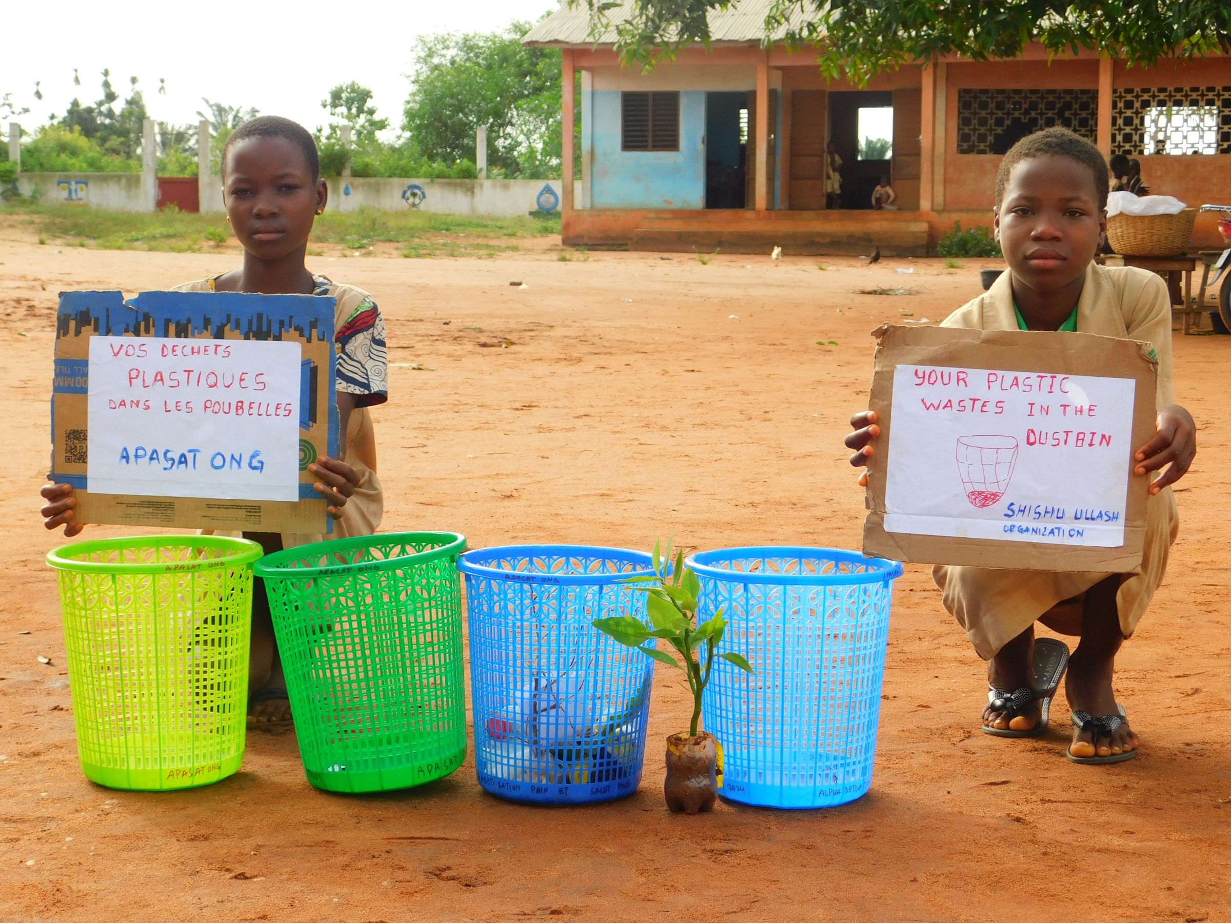 Two young children hold signs next to several dust bins