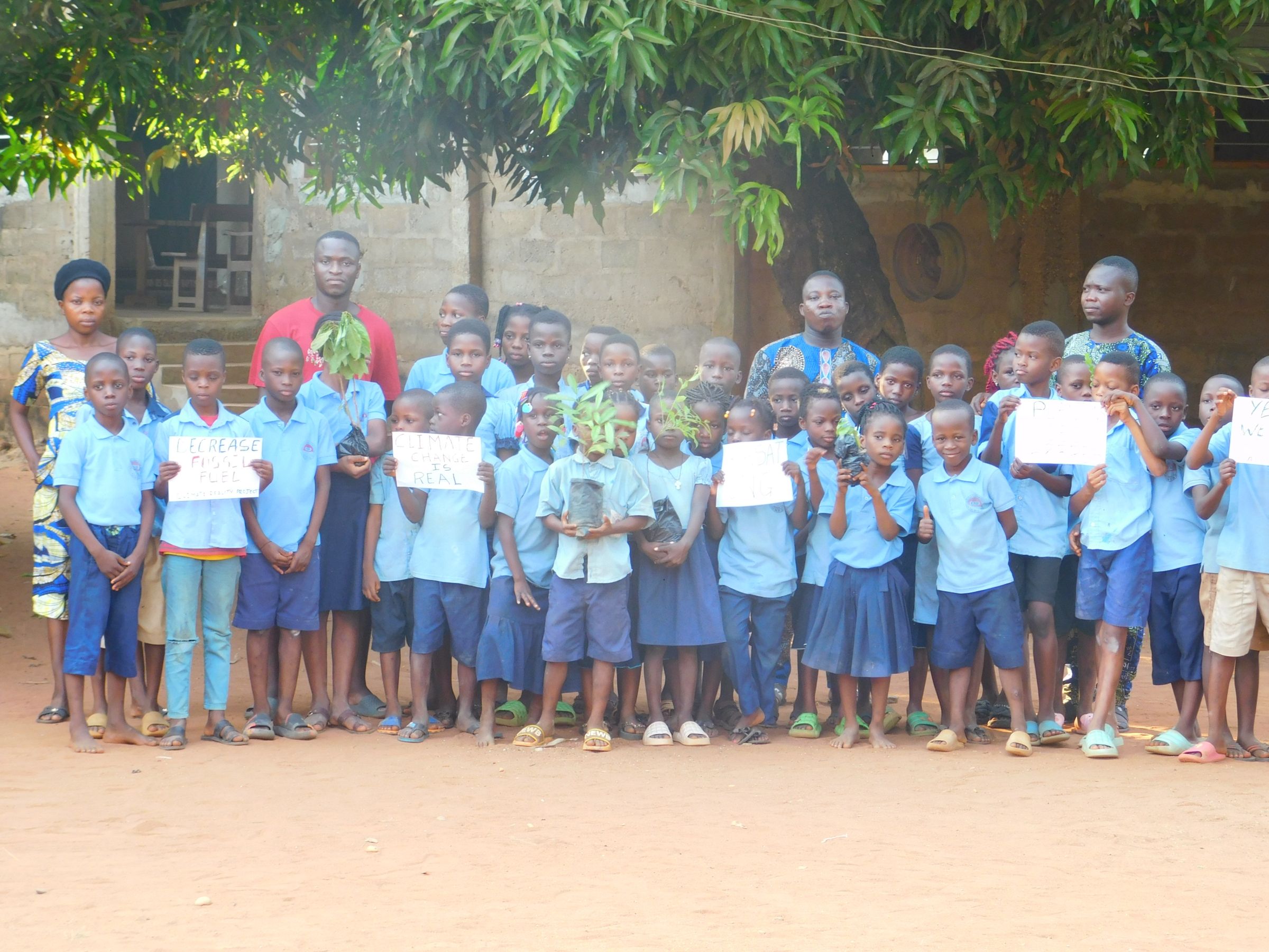 A large group of young students pose for a photo while holding signs and tree saplings