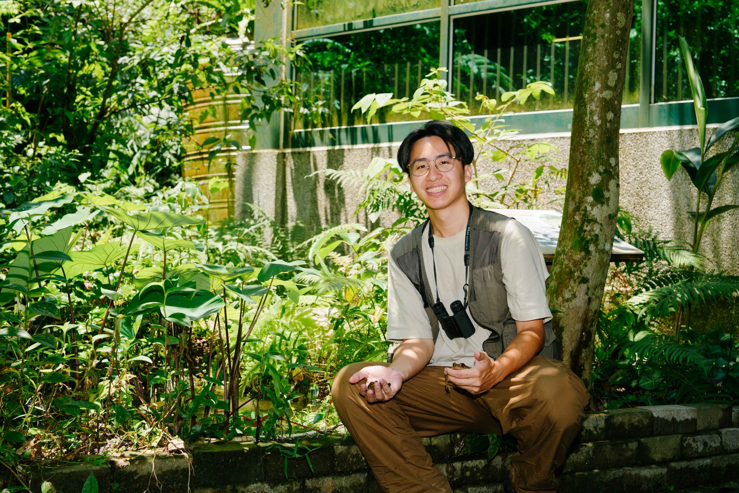Yan-Da smiling in a nature park, surrounded by green trees and plants