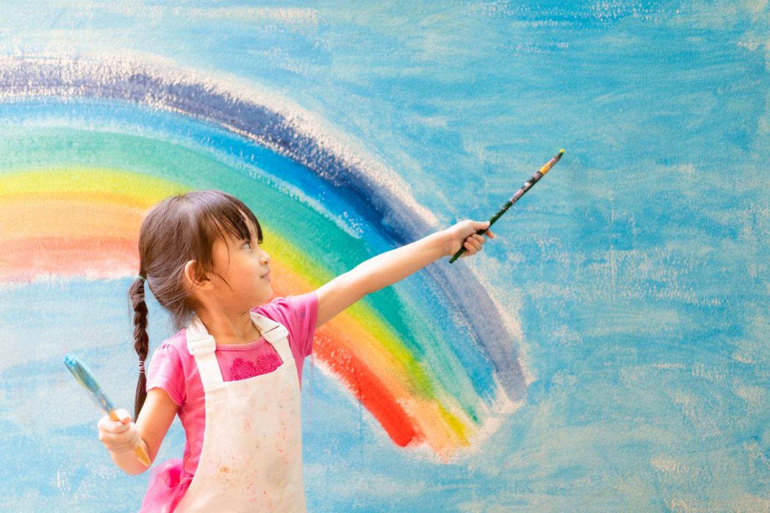 small child painting rainbow on wall